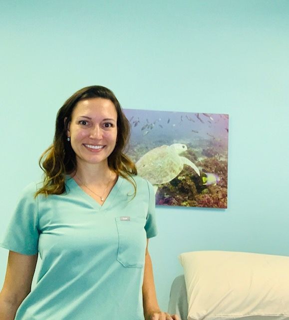 a person wearing scrubs next to a massage table with turtle picture on wall